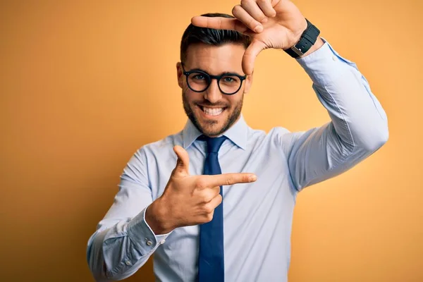 年轻英俊的生意人 戴着领带和眼镜 站在黄色的背景上 微笑着 用双手和手指制作出笑脸的框架 创意和摄影概念 — 图库照片