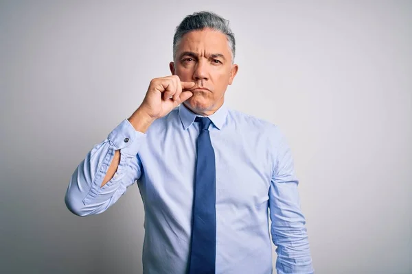 Middle age handsome grey-haired business man wearing elegant shirt and tie mouth and lips shut as zip with fingers. Secret and silent, taboo talking