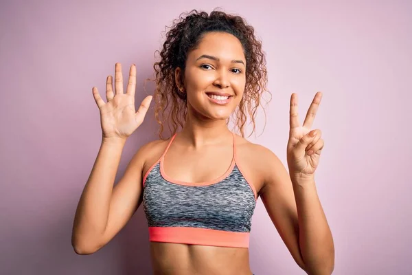 漂亮的女运动员 身穿运动服 背景粉红 手指指向七号 面带微笑 自信而快乐 — 图库照片
