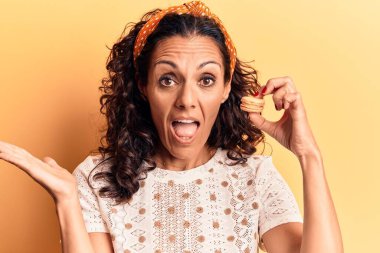 Orta yaşlı güzel bir kadın elinde makaron tutarak başarıyı mutlu bir gülümsemeyle ve kazanan bir ifadeyle kutluyor. 