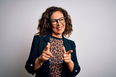 Orta yaşlı esmer iş kadını gözlüklü, izole edilmiş beyaz arka planda durup mutlu ve komik yüzlü parmakları kameraya doğrultuyor. İyi enerji ve titreşimler.