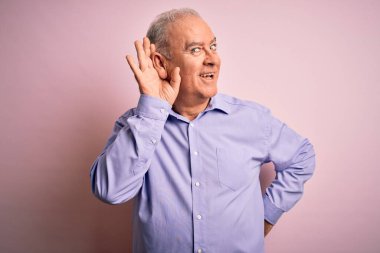 Orta yaşlı yakışıklı, beyaz bir adam pembe arka planda dikilmiş dedikodu ya da dedikodulara kulak misafiri olurken gülümsüyor. Sağırlık kavramı.