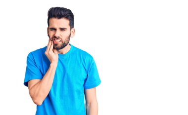 Sakallı, sıradan tişörtler giyen, diş ağrısı ya da diş hastalığından dolayı ağızlarına acı dolu bir ifadeyle dokunan genç yakışıklı bir adam. dişçi 