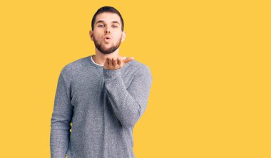 Gündelik kazak giyen genç yakışıklı bir adam kameraya bakıp havada bir öpücük savuruyor ve sevimli ve seksi oluyor. aşk ifadesi. 