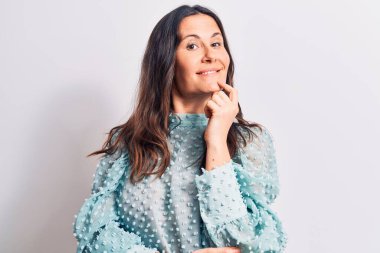 Genç ve güzel esmer kadın, günlük tişörtler giyip izole edilmiş beyaz arka planda dikiliyor. Kameraya kollarını kavuşturup, elleri çenesinde gülümsüyor. Olumlu düşünüyorum..