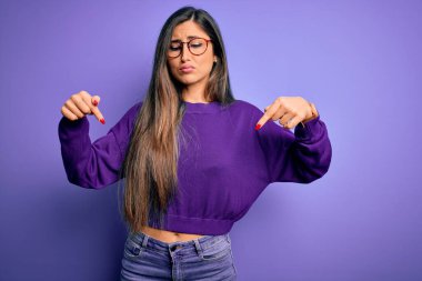 Genç, güzel, zeki bir kadın mor renkli gözlük takıyor üzgün ve üzgün görünüyor, yönünü parmaklarıyla gösteriyor mutsuz ve depresif..