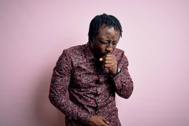 Genç ve yakışıklı Afro-Amerikalı bir adam pembe arka planda dikilmiş soğuk algınlığı ya da bronşitin belirtisi olarak öksürüyor. Sağlık hizmeti kavramı.