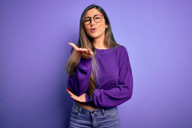 Mor izole edilmiş arka planda gözlük takan genç ve güzel bir kadın havayla öpüşen bir kameraya bakıyor. Güzel ve seksi. Aşk ifadesi.