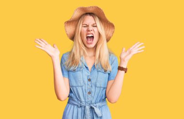 Yazlık şapka ve elbise giyen genç ve güzel sarışın kadın başarı için deli ve çılgınlığı kutluyor kollarını kaldırmış ve gözlerini kapatmış heyecanla bağırıyor. Kazanan konsept 