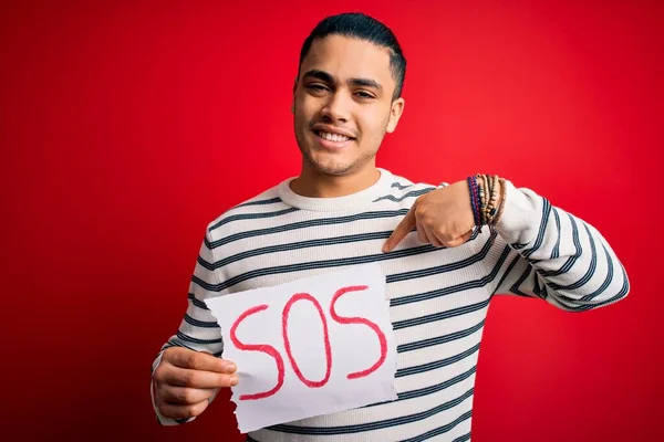 Kırmızı Arka Planda Afiş Tutmakta Zorlanan Brezilyalı Genç Bir Adam — Stok fotoğraf