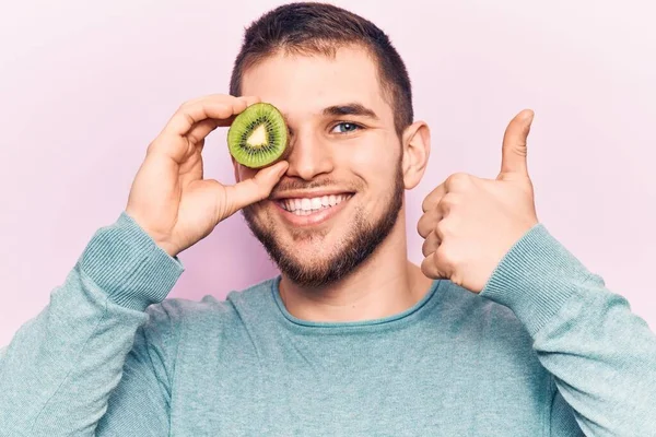 Jovem Homem Bonito Segurando Fatia Kiwi Sobre Olho Sorrindo Feliz — Fotografia de Stock