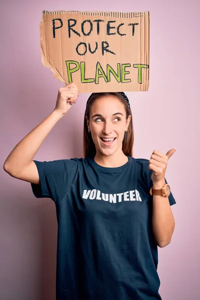 Beautiful volunteer woman doing volunteering holding banner with protect planet message pointing and showing with thumb up to the side with happy face smiling