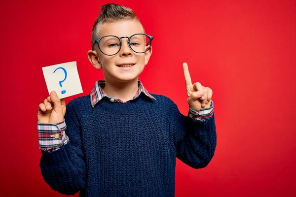 幸せな顔をしたアイデアや質問を指差す指で驚いた疑問符記号と紙のノートを保持眼鏡をかけて若い白人の子供 ナンバーワン — ストック写真