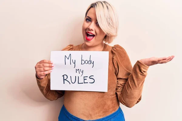 Blonde plus size woman asking for women rights holding paper with my body my rules message celebrating achievement with happy smile and winner expression with raised hand
