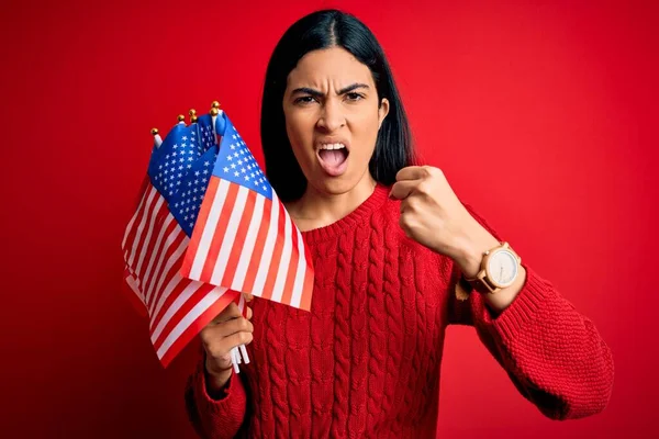 Young beautiful hispanic woman holding United States of American flag at independence day annoyed and frustrated shouting with anger, crazy and yelling with raised hand, anger concept