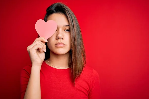 年轻美丽的黑发情妇 身披红纸心形 背景孤寂 神气十足 脸上挂着严肃严肃的表情 — 图库照片