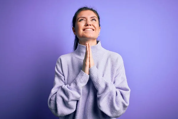 Young beautiful woman with blue eyes wearing casual turtleneck sweater over pink background begging and praying with hands together with hope expression on face very emotional and worried. Begging.