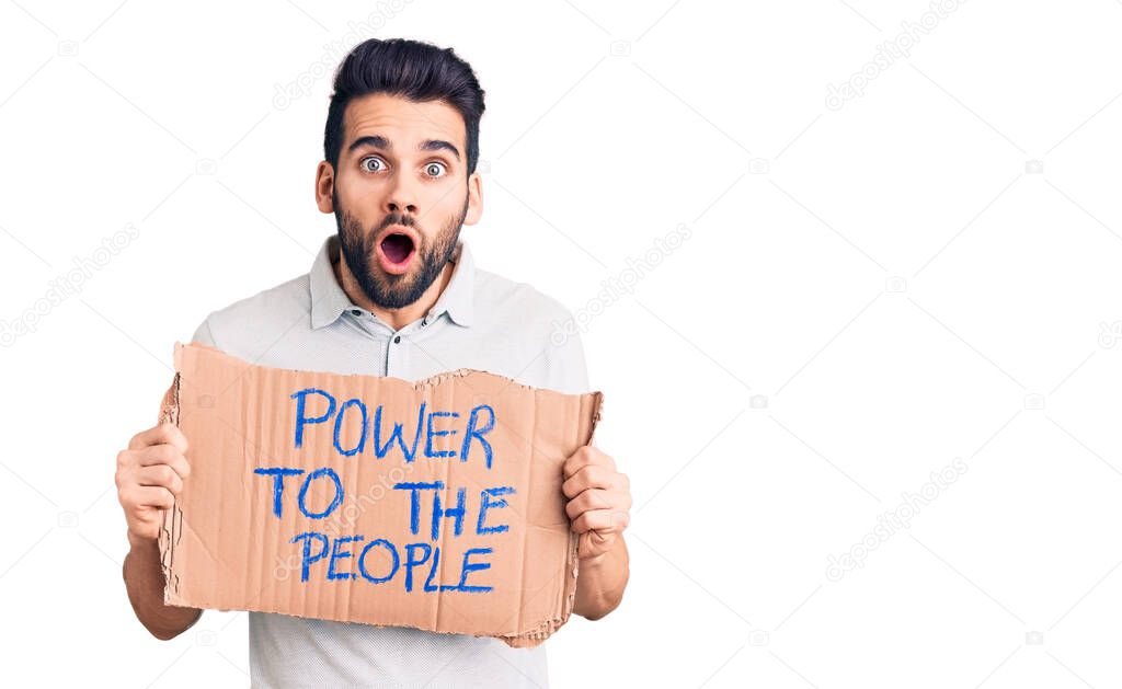 Young handsome man with beard holding power to the people cardboard banner scared and amazed with open mouth for surprise, disbelief face 