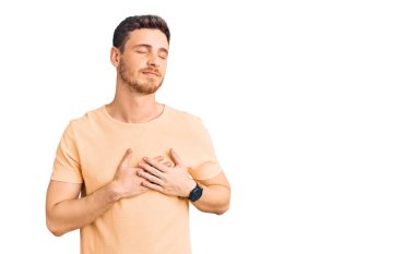 Ayılı yakışıklı genç adam, gündelik sarı tişört giyiyor, elleri göğsünde, gözleri kapalı gülümsüyor ve yüzünde minnet ifadesi var. sağlık kavramı. 