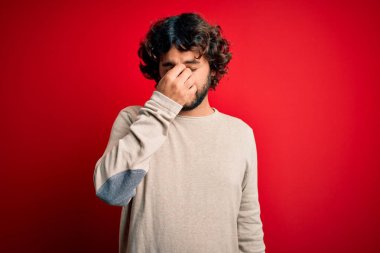 Sakallı, sıradan bir süveter giyen, kırmızı arka planda dikilen, burnu ve gözleri ovuşturan, yorgun ve başı ağrıyan genç yakışıklı bir adam. Stres ve hüsran kavramı.