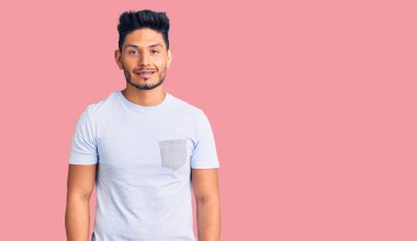 Yakışıklı Latin Amerikalı genç adam sıradan kıyafetler giyiyor ve yüzünde mutlu ve havalı bir gülümseme var. şanslı kişi. 