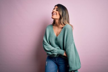 Moda kıyafetleri giyen genç ve güzel bir kadın. Manken, sokak tarzı giyiniyor. Pembe arka planda dikiliyor.