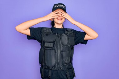 Mor arka planda kurşun geçirmez yelek giyen genç bir kadın. Gözleri neşeli ve komik gülümseyerek kapatıyor. Kör kavram.