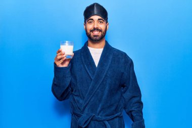 Uyku maskesi ve bornoz takan genç İspanyol adam süt içiyor. Pozitif ve mutlu görünüyor. Kendine güvenen bir gülümsemeyle dişlerini gösteriyor. 