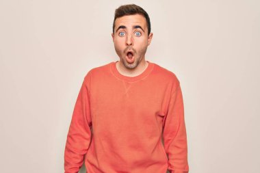 Mavi gözlü genç adam beyaz arka plan üzerinde duran sıradan bir süveter giyiyor. Şaşırmış ve korkmuş bir ifade, korku ve heyecanlı bir yüz ifadesi var..