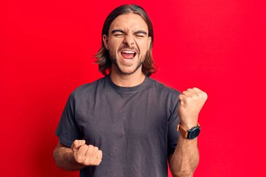 Gündelik giysiler giyen genç yakışıklı adam şaşkınlık ve şaşkınlık içinde başarıyı kollarını kaldırarak ve gözlerini kapatarak kutluyor. 