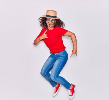 Orta yaşlı, güzel İspanyol bir kadın, sıradan kıyafetler giyiyor ve mutlu bir şekilde gülümsüyor. Yüzünde gülümsemeyle zıplıyor boynuz işareti yapıyor parmakları beyaz arkaplanda