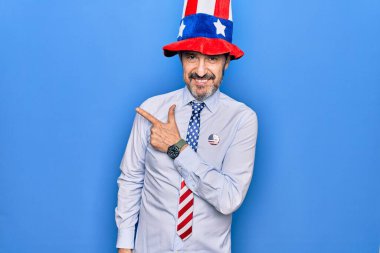 Orta yaşlı, yakışıklı, vatansever, şapkalı ve kravatlı, mavi arka planda gülümseyen, el ve parmak uçlarında neşeli bir adam.