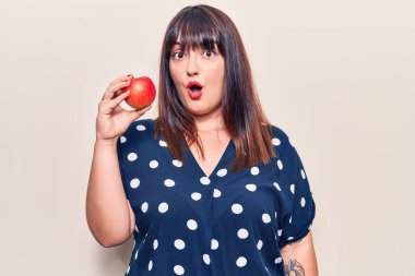 Genç ve iri yarı bir kadın kırmızı elma tutuyor. Korkmuş ve ağzı açık, şaşırmış ve şaşırmış. 