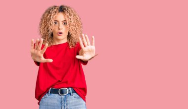 Kıvırcık saçlı, gündelik kırmızı tişörtlü genç sarışın kadın avuç içi hareketlerini durduruyor, kızgın ve hayal kırıklığına uğramış yüz ifadesi takınıyor. 