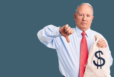 Üst düzey yakışıklı, gri saçlı, şık kıyafetler giyen, elinde kızgın yüzlü para çantası tutan, olumsuz işaretli, baş parmakları aşağıda, reddedilme konsepti olan bir adam. 