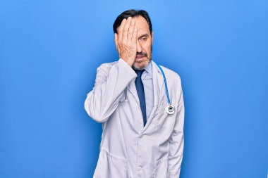 Paltolu ve steteskop takmış orta yaşlı yakışıklı bir doktor. Mavi arka plan üzerinde. Yanlışlıkla el ele tutuşarak şaşırmış. Unuttum, kötü hafıza konsepti.