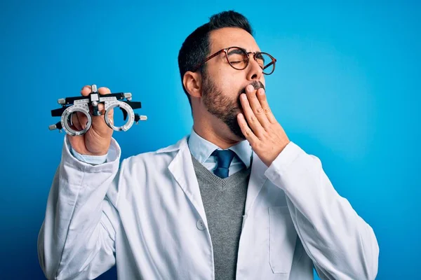 Młody Przystojny Optyk Brodą Trzymający Okulary Optometryczne Nad Niebieskim Tłem — Zdjęcie stockowe