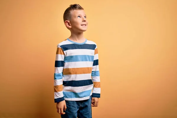 青い目をした若い白人の子供は 顔に笑顔で横に見える黄色の背景にカラフルなストライプのシャツを着て 自然な表情 自信を持って — ストック写真