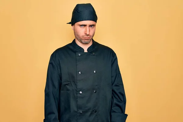 Young handsome cooker man with blue eyes wearing uniform and hat over yellow background skeptic and nervous, frowning upset because of problem. Negative person.