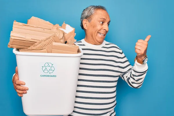 ゴミを持っている高齢者のリサイクルは 青い背景を指して 幸せな顔を笑顔で親指で横に示す上でリサイクルすることができます — ストック写真