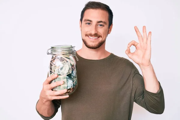 Joven Hombre Guapo Sosteniendo Frasco Con Ahorros Haciendo Signo Con — Foto de Stock