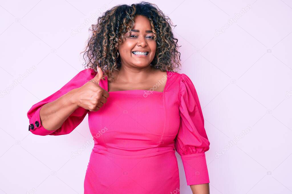 Young african american plus size woman wearing casual clothes smiling happy and positive, thumb up doing excellent and approval sign 