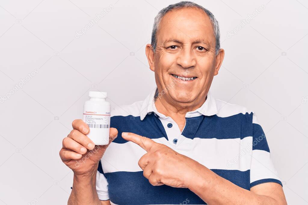 Senior man with grey hair holding bottle of pills smiling happy pointing with hand and finger 