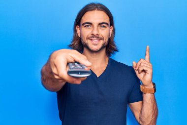 Elinde televizyon kumandası olan yakışıklı bir adam bir fikre ya da soru işaretine şaşırdı. 