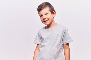 Hoş sarışın çocuk günlük kıyafetler giyiyor. Pozitif ve mutlu görünüyor. Kendine güvenen bir gülümsemeyle dişlerini gösteriyor. 