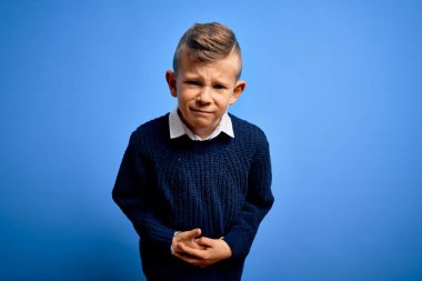 Mavi gözlü küçük beyaz çocuk mavi arka plan üzerine mavi süveter giyiyor ve elleri karnında, çünkü hazımsızlık, acı verici bir hastalık var. Ache kavramı.