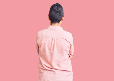 Kısa saçlı, sıradan kıyafetler giyen, kollarını kavuşturup arkasına bakan genç bir kadın. 