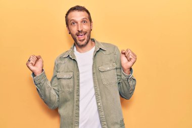 Gündelik giysiler giyen genç yakışıklı adam şaşkınlık ve şaşkınlık içinde kollarını kaldırarak ve gözlerini açarak başarıyı kutluyor. Kazanan konsept. 