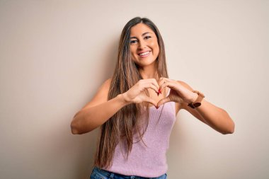 Uzun saçlı güzel esmer kadın izole edilmiş arka planda duruyor. Aşkla gülümsüyor. Elleriyle kalp sembolü ve şekli gösteriyor. Romantik konsept.