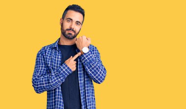 Gündelik kıyafetler giyen genç İspanyol adam saati, sabırsızlığı ve rahat bir ifadeyle kameraya bakmayı işaret ediyor. 